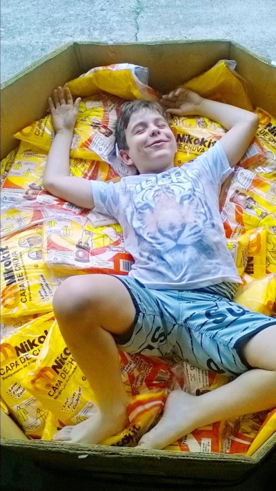 Menino sorrindo deitado sobre embalagens de capas de chuva Nikokit dentro de uma grande caixa de papelão